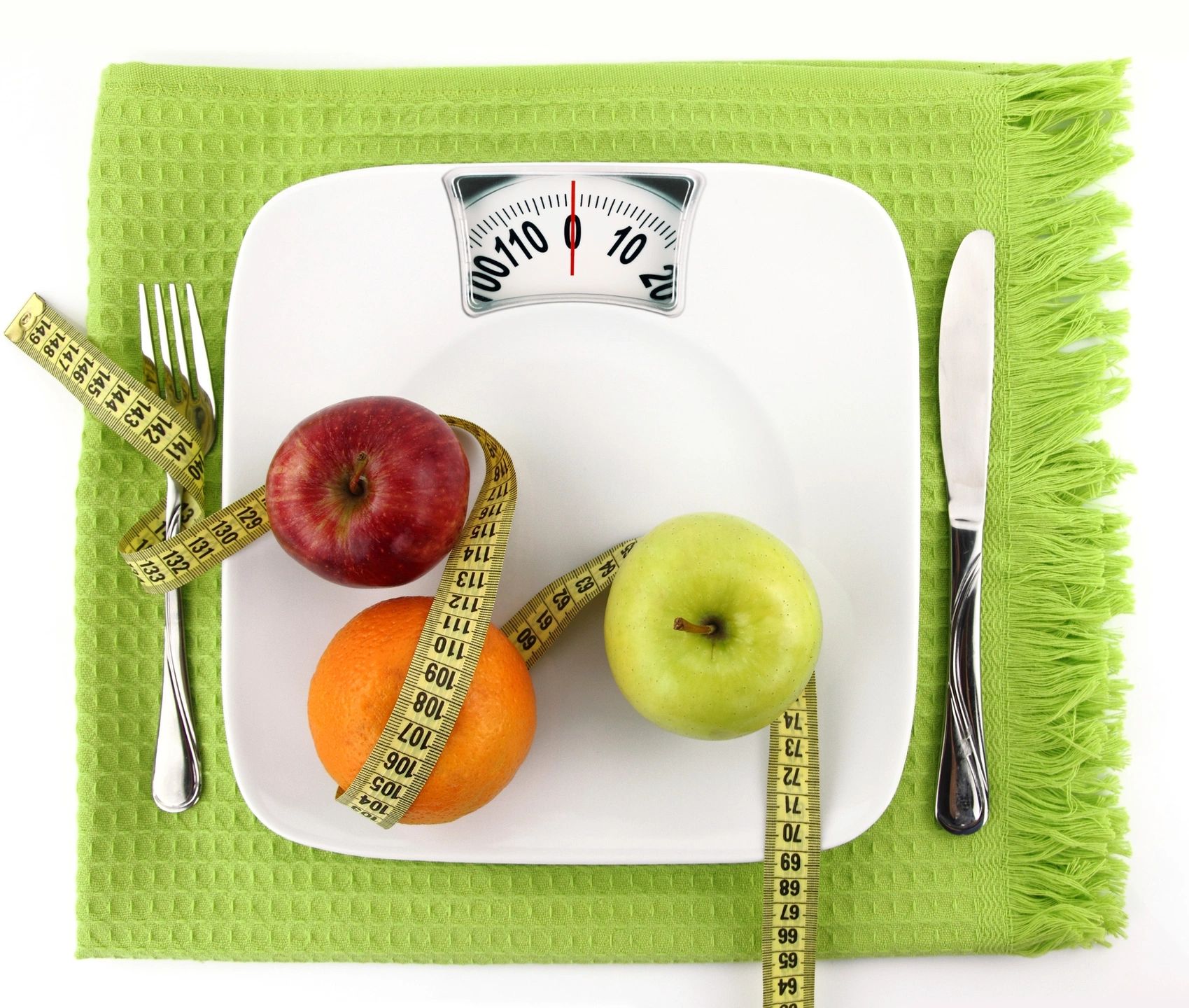Apples and a measuring tape on a weighing scale with a fork and knife